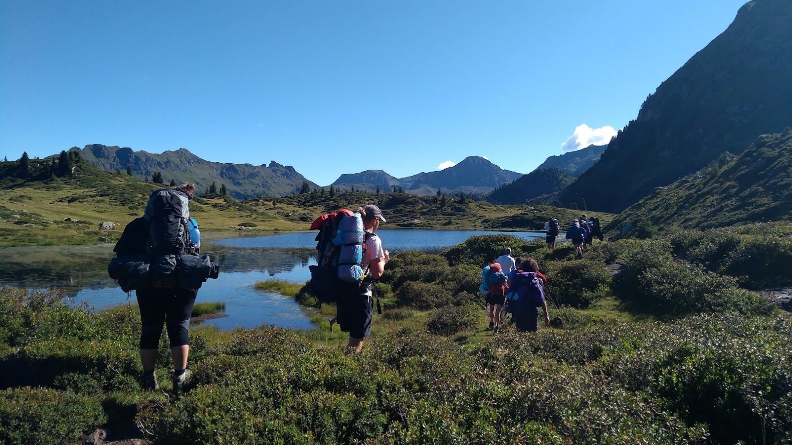 Ragazzi con lo zaino in cammino su un sentiero tra laghetti alpini