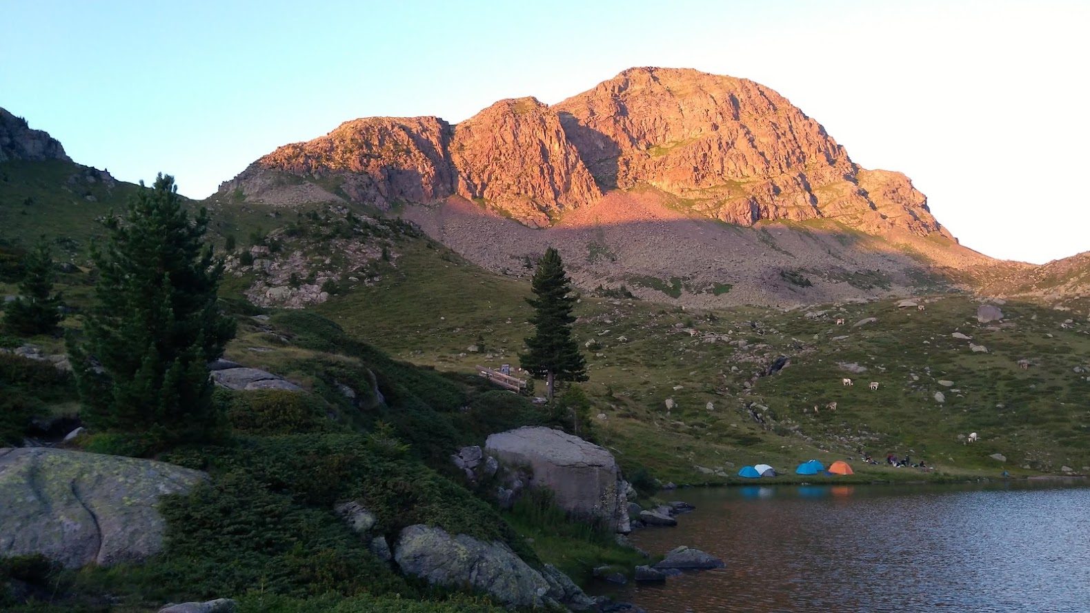 Tende in riva a un lago alpino, con la cima illuminata dal tramonto